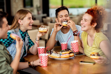 Group of cheerful friends eating donuts in a cafe.