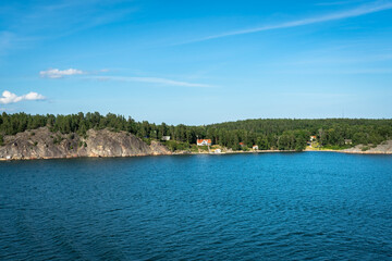 Fototapeta na wymiar Amazing panorama of blue Baltic sea bay. View from the top of cruiser ship. Rocky shores of Scandinavia with colorful old traditional houses. Forest pine islands. 