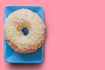 On a blue saucer is a sweet, fresh doughnut with a white glaze. The view from the top. Pale pink background. Free space for copying.