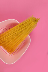 Różowy durszlak z surowym zbożowym makaronem na spaghetti bolognese na różowym tle