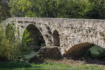 Ancient stone bridge. Travel to Spain. Roman building. Medieval stone construction. Historical memo. Camino de Santiago. Crossing the river. Transport connection. Bridge with arches.