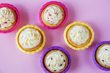Multi-colored cupcakes with cream on a pink background with different ribbons. Festive background with free space. Holiday baking. Birthday baking.