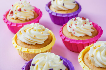 Multi-colored cupcakes with cream on a pink background with different ribbons. Festive background with free space. Holiday baking. Birthday baking.