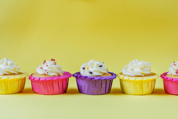 Four multi-colored cupcakes with cream on a yellow background with different ribbons. Festive background with free space. Holiday baking. Birthday baking.