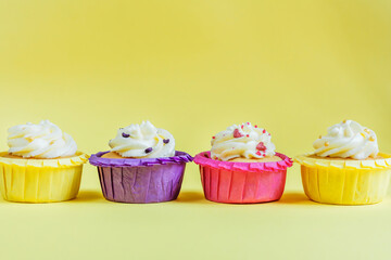 Four multi-colored cupcakes with cream on a yellow background with different ribbons. Festive background with free space. Holiday baking. Birthday baking.