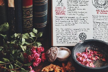 Wiccan witch altar with an open book of shadows with hand written spell in it, ready for spell casting. Grimoire page with symbols and drawings. Old vintage books, dried flowers, salt ingredients