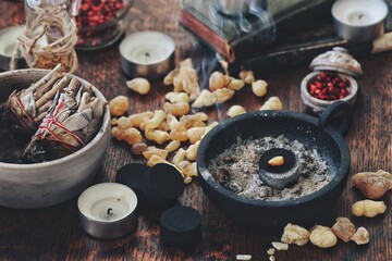 Peace of frankincense resin incense burning on charcoal as air cleansing ceremony on a wiccan witch altar. Honoring air element. Lots of light yellow Yemen frankincense on a table. Sage smudge sticks 