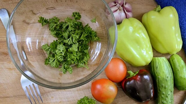Fresh sliced vegetables are on the table, ready for slicing salad. Bulgarian pepper, tomato, herbs, cucumber, garlic for cooking vegetable dishes. A knife and fork next to a glass bowl .