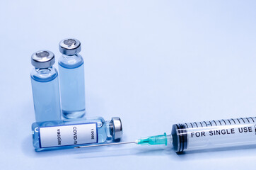Coronavirus vaccine in glass vials with a syringe on a blue background.