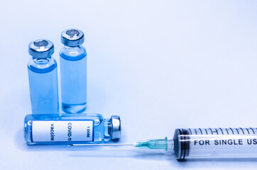 Coronavirus vaccine in glass vials with a syringe on a blue background.