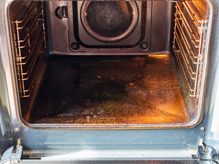 cleaning oven in home kitchen - inside view of dirty oven with carbon deposits on bottom and walls