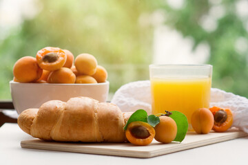 Healthy and tasty breakfast, healthy food concept. Ripe apricots, a glass of juice and a fresh crunchy croissant on a wooden stand with a towel on a white wooden table in the garden. Copyspace