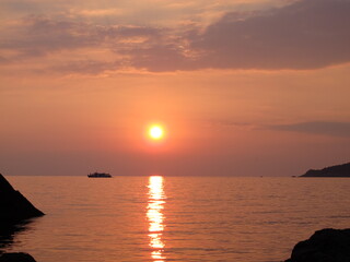 Scenic view of bright golden setting sun and reflection in sea water, silhouette of a pleasure boat on the horizon, sunset on the seaside, clouds, sky, sea and sun in orange-pink tones