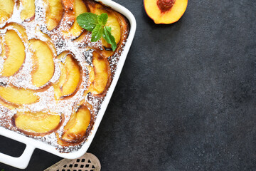 Delicate cake with peaches sprinkled with powdered sugar on a black concrete background