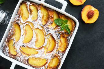 Delicate cake with peaches sprinkled with powdered sugar on a black concrete background
