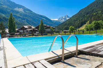 Pool and crystalline waters in a green valley with mountain peaks in the background. Italian alps