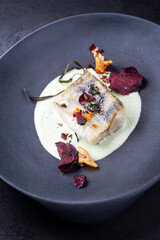 Traditional fried skrei filet cod fish with vegetable chips and algae in a lemon coconut sauce offered as close-up in a modern design plate with copy space