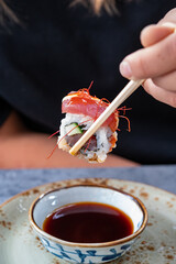 Japanese food, eating sushi or sashimi made from rice with salmon, avocado, cucumber, red fish caviar, tempura shrimps with chopsticks