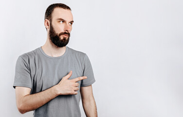Handsome brunette man with a beard points a finger at a place for advertising on a white background