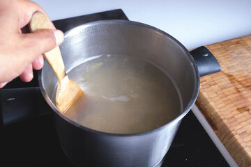 Cooking with boiling water in an inox pan on a domestic kitchen mixing with a wooden spoon