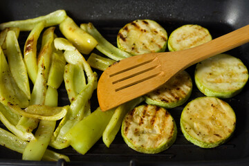 Grilled vegetables in a pan. Close-up of zucchini and sweet peppers. Wooden spatula for cooking