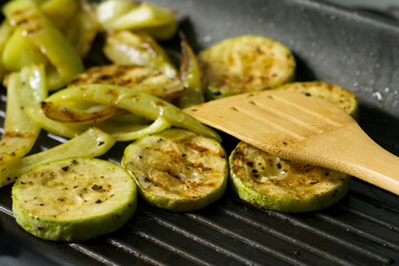 Grilled vegetables in a pan. Close-up of zucchini and sweet peppers. Wooden spatula for cooking