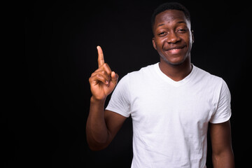 Happy young handsome African man against black background