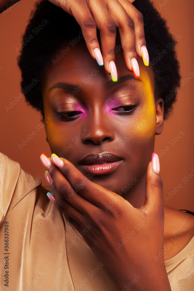 Wall mural young pretty african girl with bright colorful makeup and manicure posing cheeful on brown backgroun