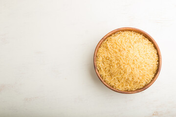 Wooden bowl with raw golden rice on a white wooden background. Top view, copy space.