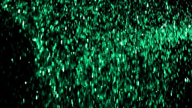 Green glitter particles falls against black background shot in slow motion at 480fps 