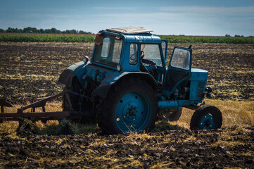 Fototapeta premium blue old tractor plowing field side view