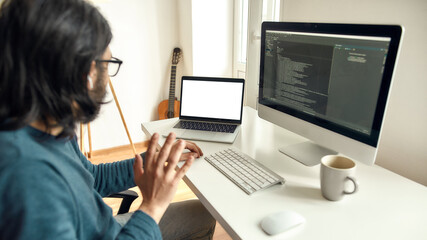 Video conference. Male web developer looking at webcam and waving while while sitting at his workplace and working from home, writing code on desktop computer