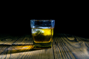 A glass of whiskey on a dark wood table on a dark background.