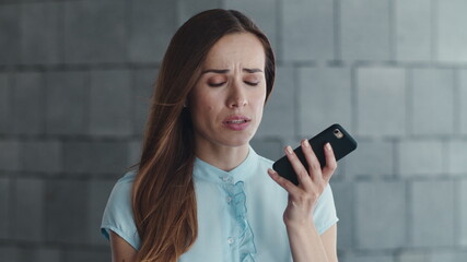 Upset female employee recording voice message on cellphone outside