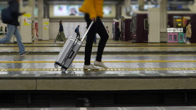 Passenger woman walk with one trolley case at empty platform, large Umeda railway station. Few people run at background, hurry to catch train departure, super slow motion shot
