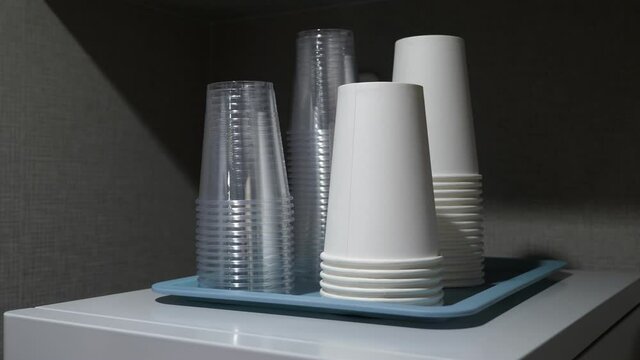 Woman pick up one new plastic cup, white paper cups in stack near. Close up shot of empty disposable cups standing upside down in pile, small tray at top of vending machine