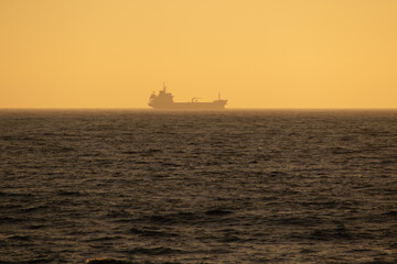 Obraz premium Large cargo ship sailing smoothly in the ocean during a wonderful sunset, Portugal
