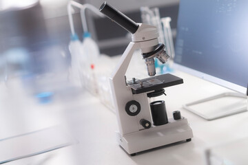 A microscope in a modern laboratory with a medical screen behind.