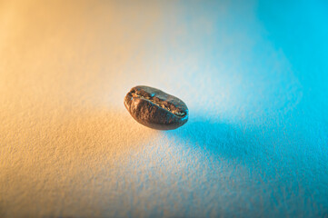 Closeup of a single roasted coffee bean, isolated on an orange and blue colored background