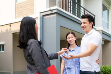 Asian happy smile young couple take keys new big house from real estate agent or realtor in front of their house after signing contract agreement