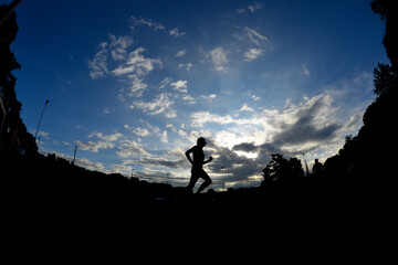 Ein Sportler läuft auf der Laufbahn in einem Stadion und bildet sich als Silhouette vor dem Morgenhimmel ab.