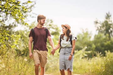 Couple Hiking Along Woodland Path. Happy loving man and woman on holiday walking together. Active lifestyle concept. Young people walking with backpacks on country road outdoors