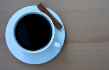 A white cup of coffee with a cinnamon stick on a wooden table