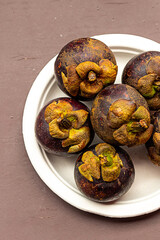 mangosteen - tropical fruit of Thailand. Round hard brown crust lilac tastyю. A lot of fruit is on the plate