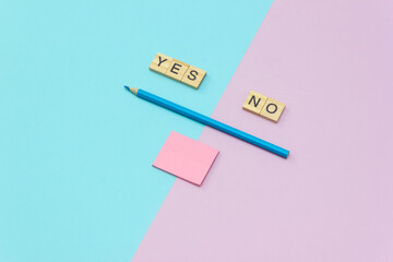 Words Yes No. Wooden blocks with lettering, blue pencil and pink block for notes on multicolor background. Top view, layout