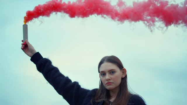 Girl holding smoke bomb in hand at street protest. Woman using smoke grenade