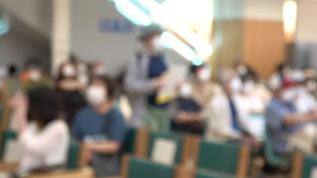 Blurred shot of patients with mask waiting in the crowded lobby at hospital in Japan. Social distancing. 4K