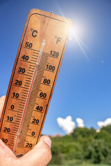 Thermometer during hot summer showing high temperature. Human hand holding a wall thermometer against nature background, concept of global warming. Close up, vertical image, copy space for text.
