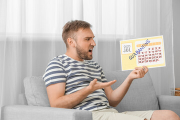Angry man with calendar dreaming about vacation during quarantine at home