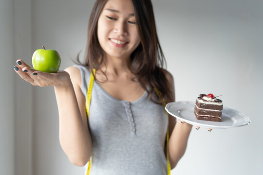 Choose right food for you health. Person eat dessert holding green apple and cake to compare calories as sweet menu to eat during diet.